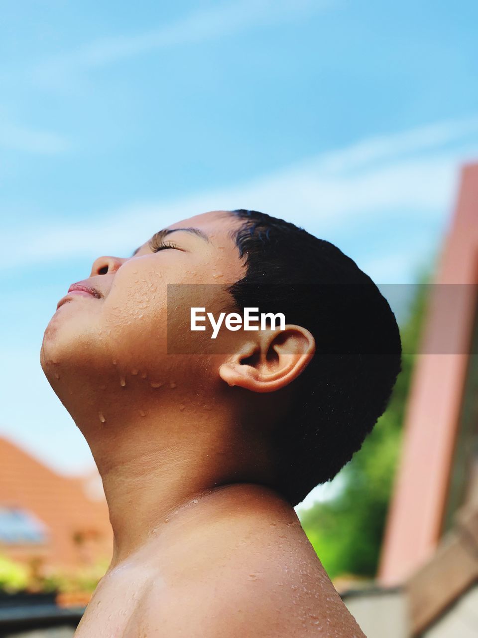 Close-up of boy standing with eyes closed against sky during rainy season