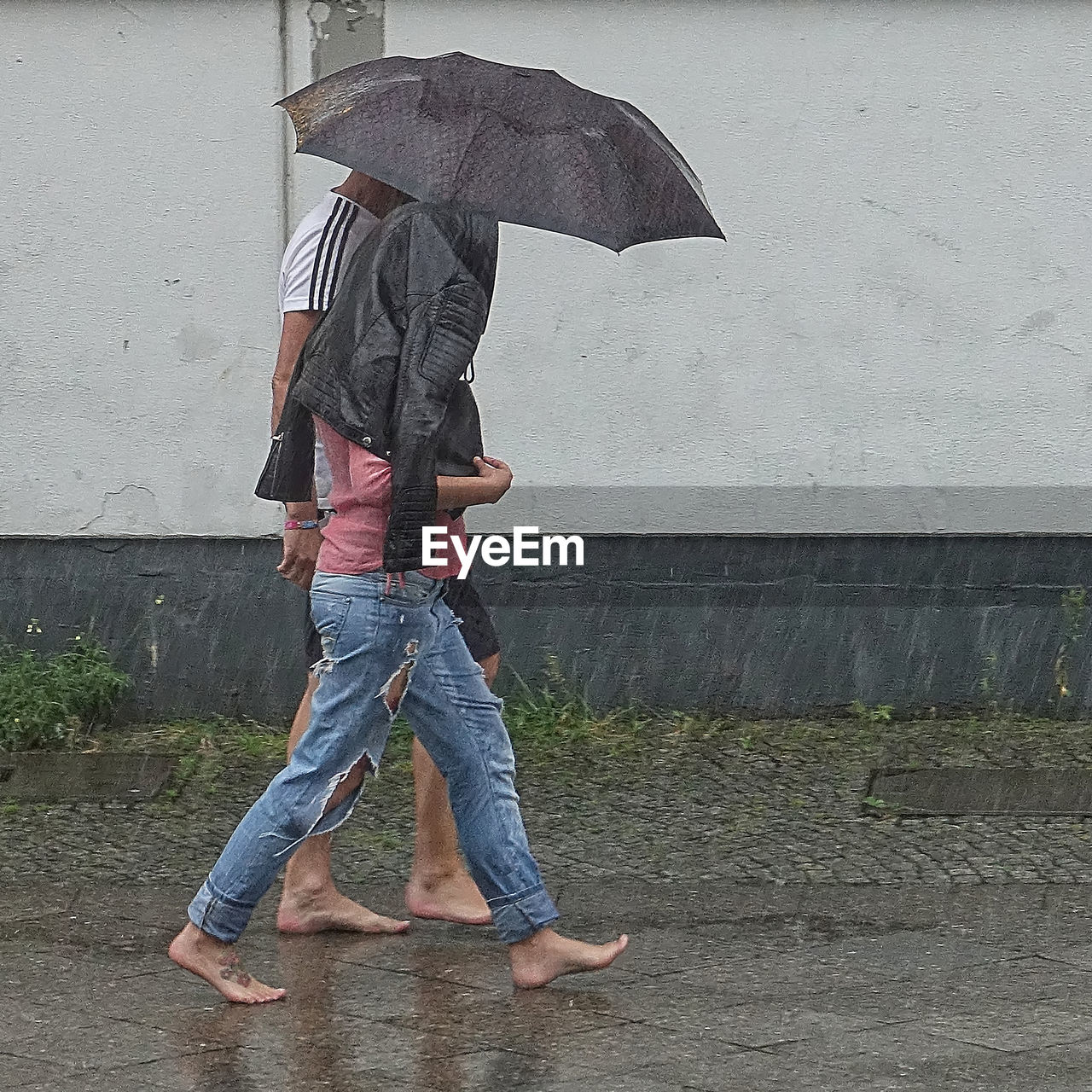 LOW SECTION OF MAN WITH UMBRELLA WALKING ON WET RAINY SEASON