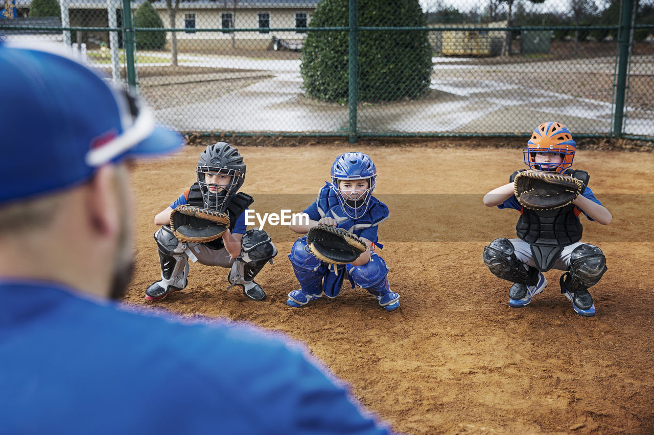 Rear view of coach training baseball catchers on field