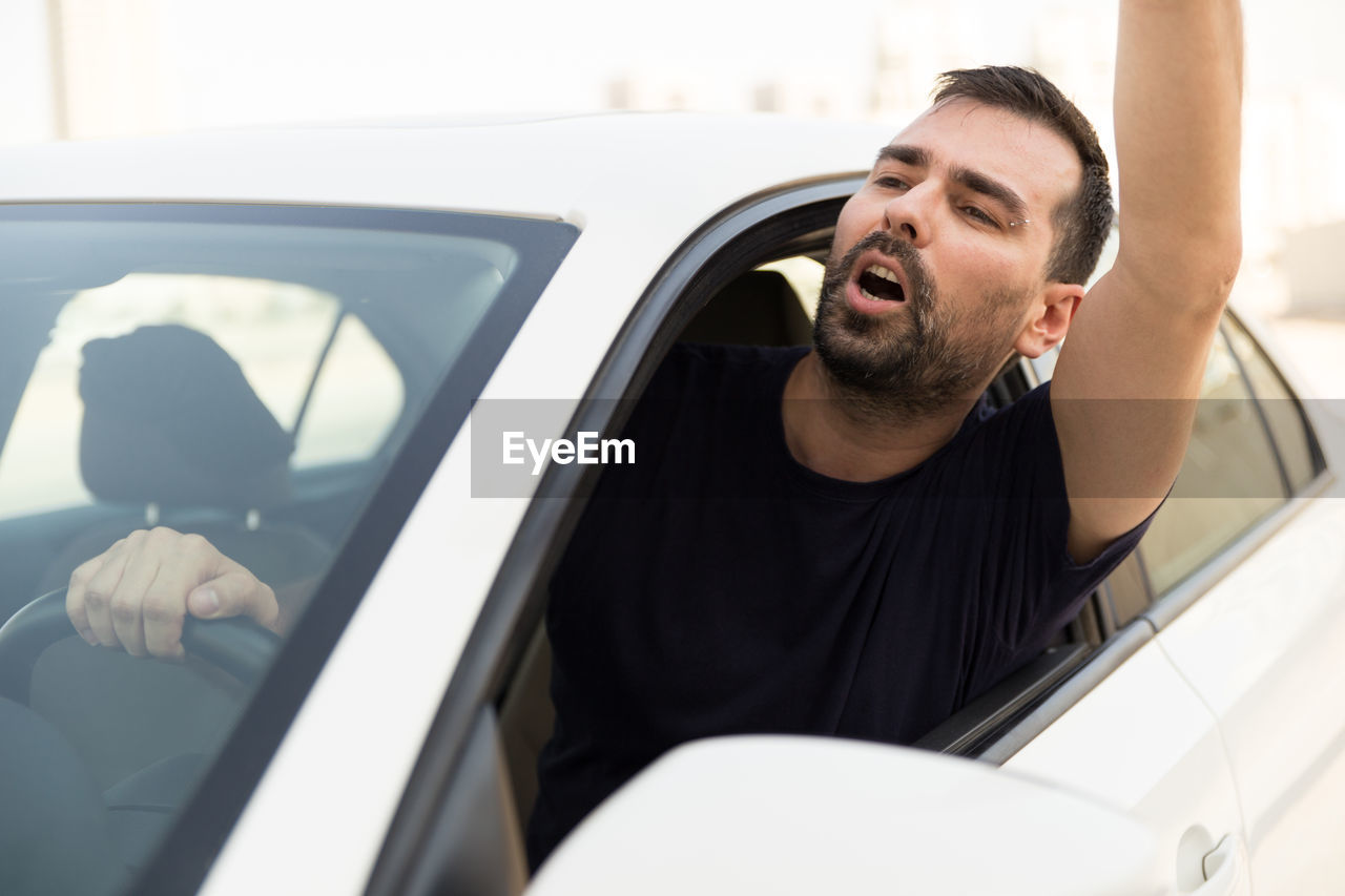 Frustrated man shouting through window while traveling in car