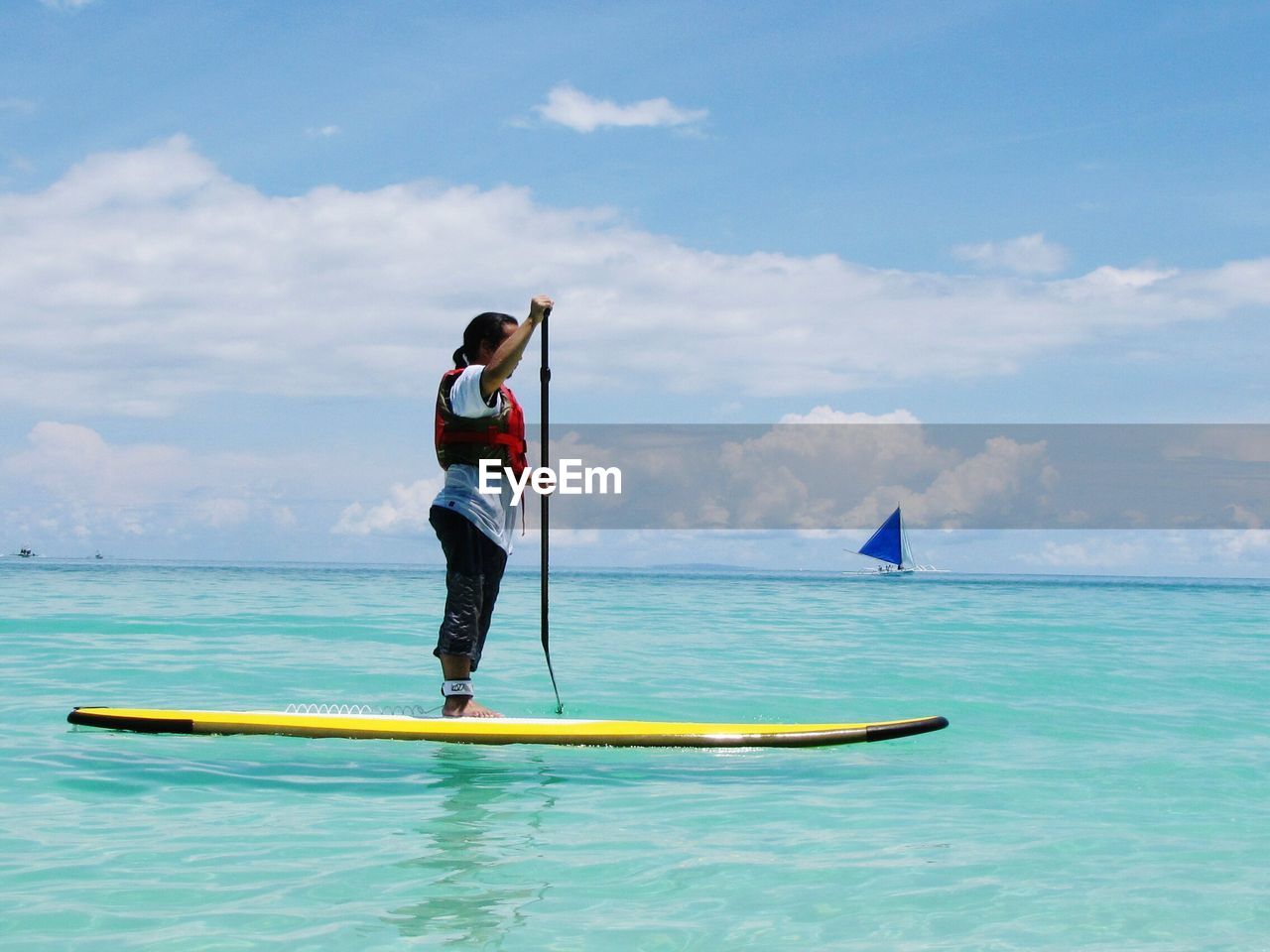 Full length of woman paddle boarding on sea against cloudy sky