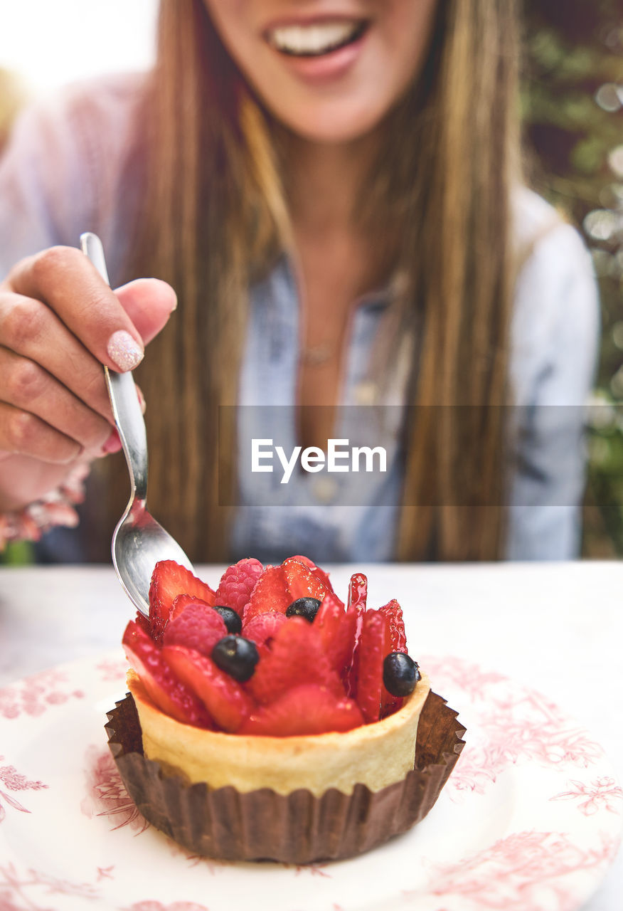 Young woman tasting strawberry-topped cake, selective focus.