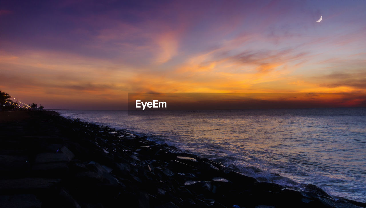 Scenic view of sea against cloudy sky during sunset