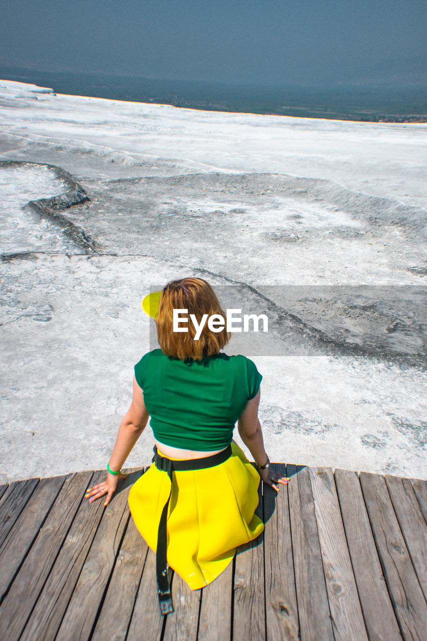 Rear view of woman sitting on boardwalk