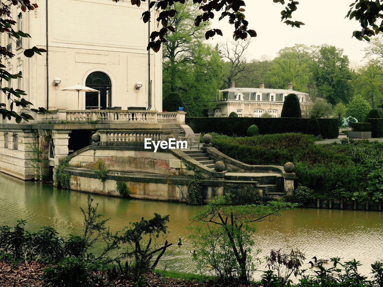 Arch bridge over lake by buildings against sky