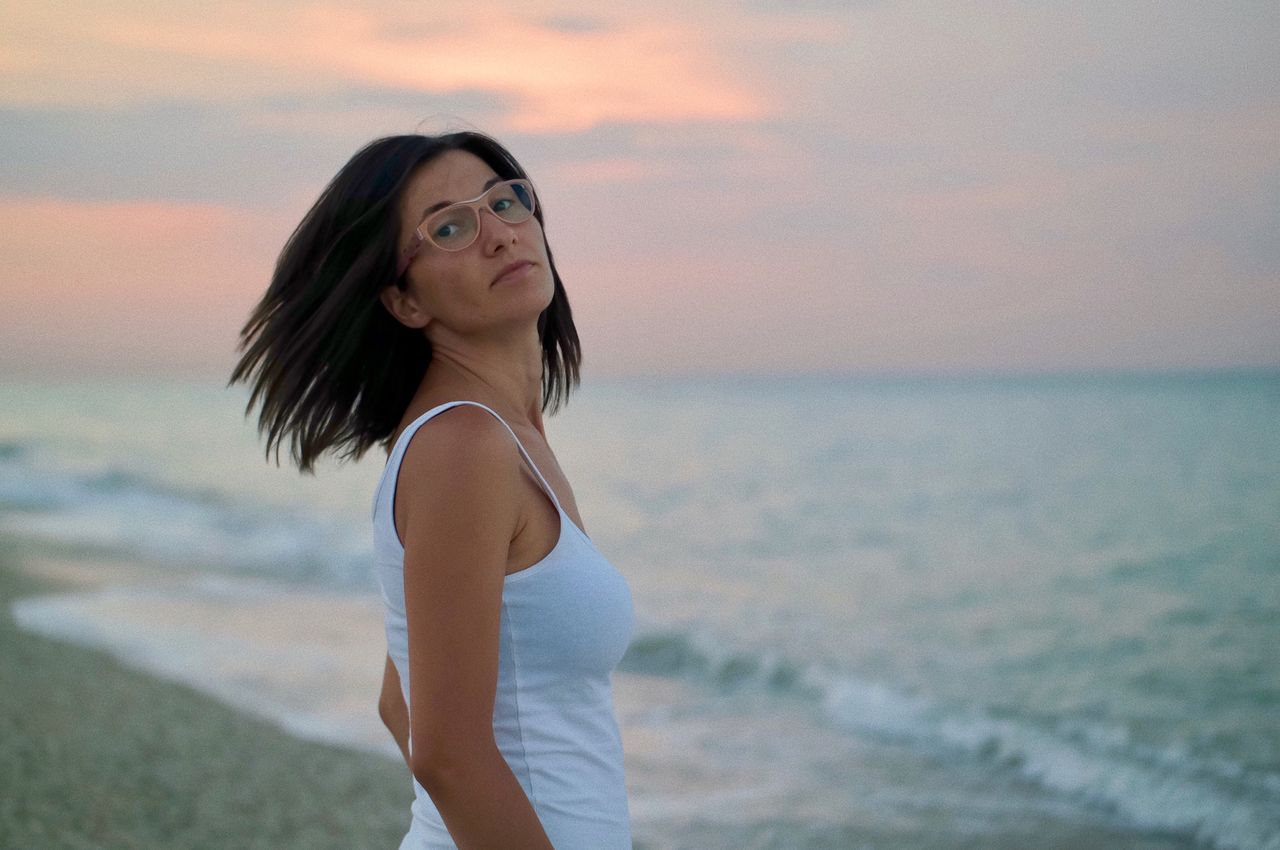 Portrait of woman standing on shore at beach during sunset