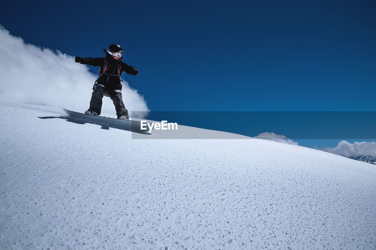 Young sportswoman woman on a snowboard rolls down a snowy slope against a blue sky on a sunny day