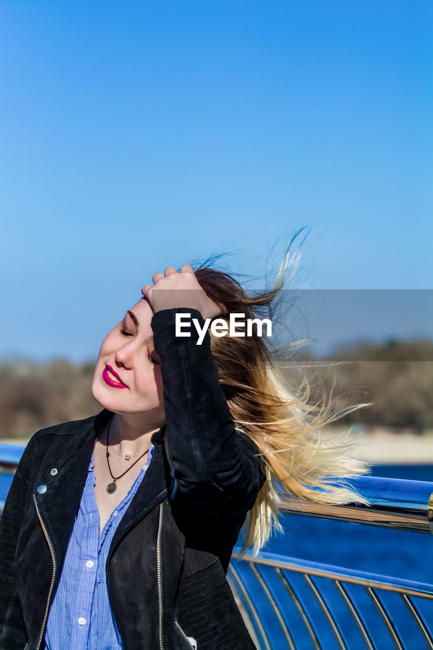 Smiling woman with hand in hair against sky