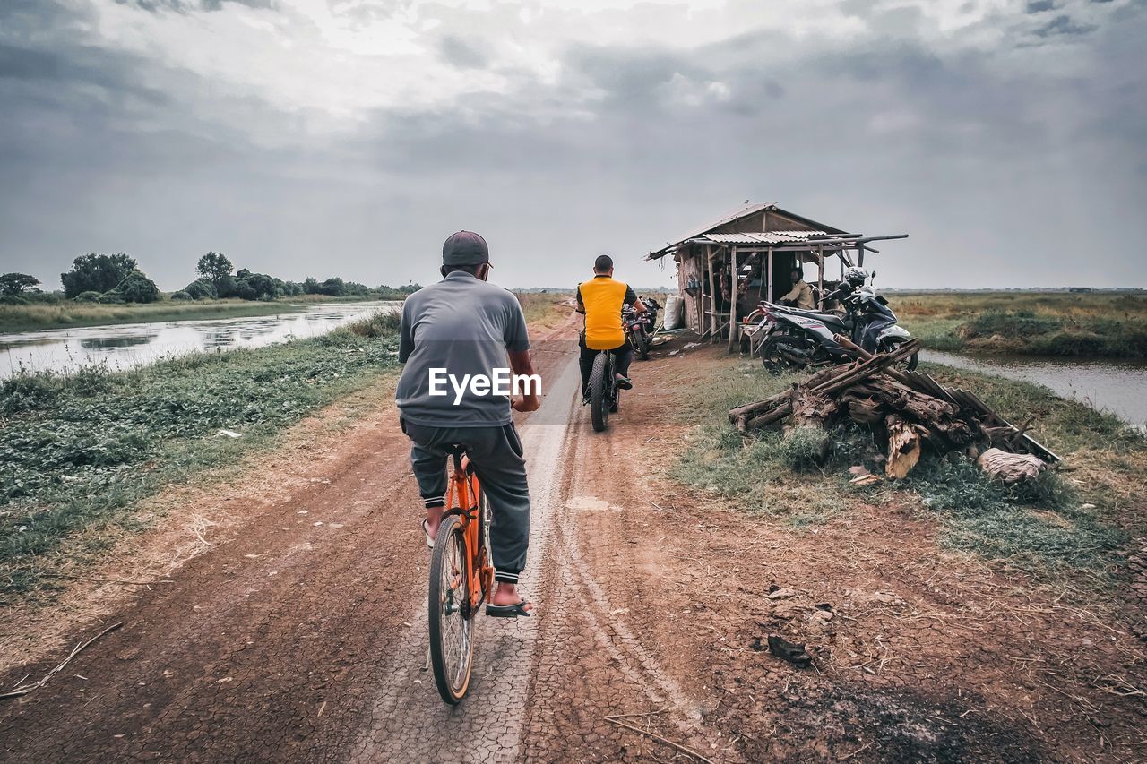 Rear view of man riding bicycle on road against sky