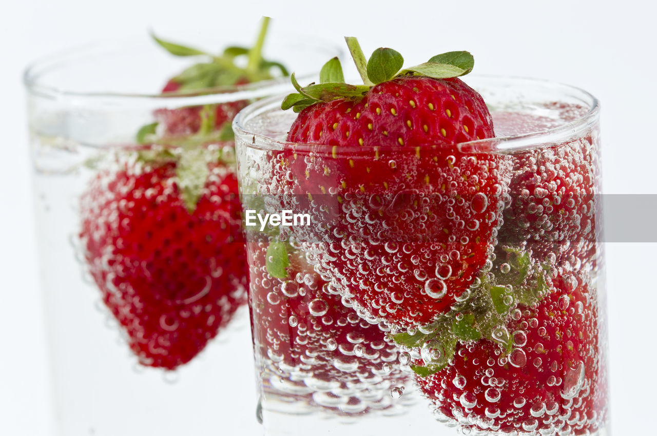 Close-up of strawberries in drinks against white background