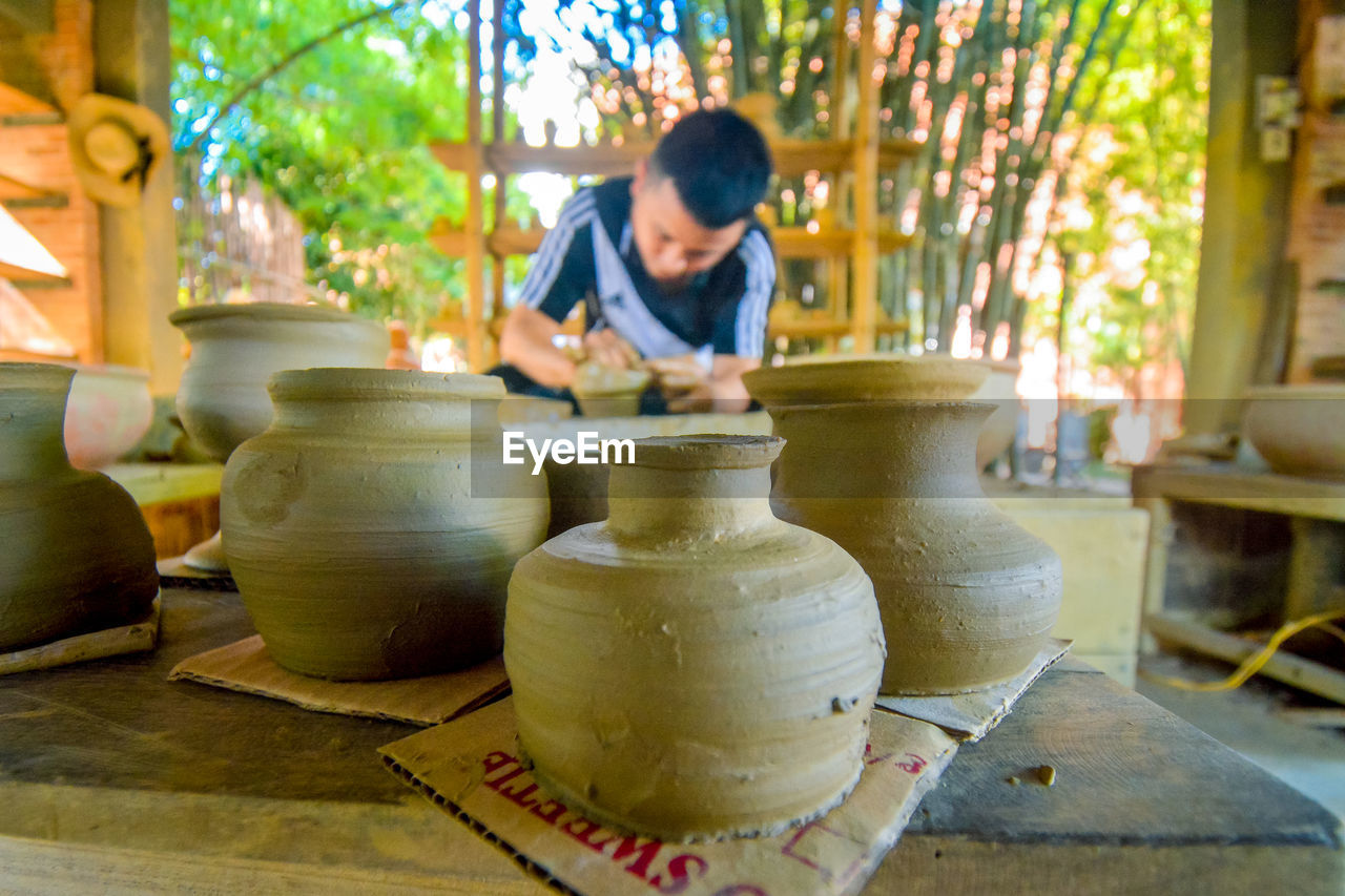 potter's wheel, pottery, craft, art, ceramic, clay, working, creativity, occupation, adult, skill, earthenware, one person, craftsperson, workshop, making, vase, craft product, expertise, men, nature, indoors, business, day, small business, young adult, pitcher - jug, plant, concentration, lifestyles