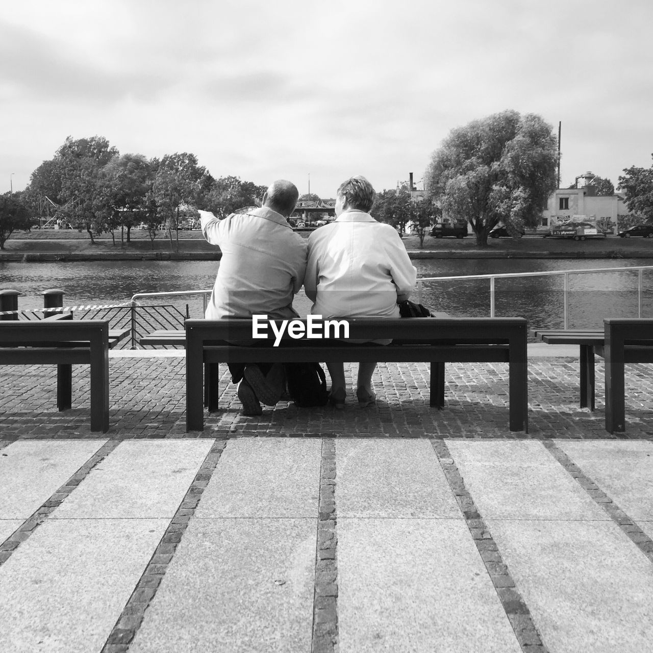 Rear view of couple sitting on bench by lake at park