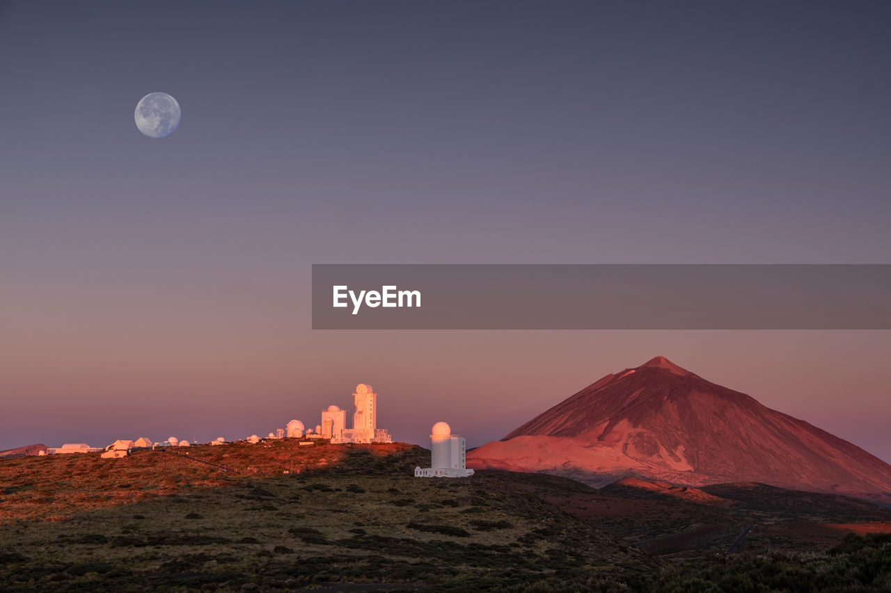 Observatory in teide nationalpark with volkano inthe back at sunrise with moon above.