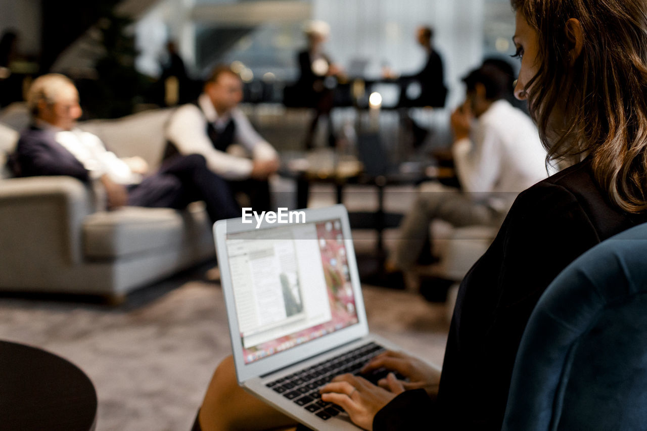 Businesswoman using laptop with colleagues sitting in background at office