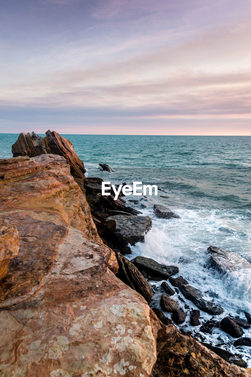 Scenic view of rock by sea against sky during sunset