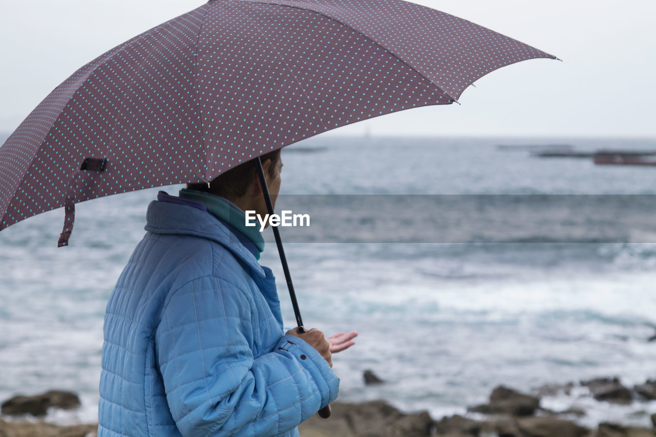 Woman in coat and umbrella in front of the coast