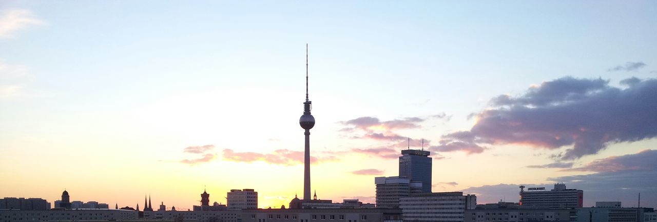 Communications tower in city against cloudy sky