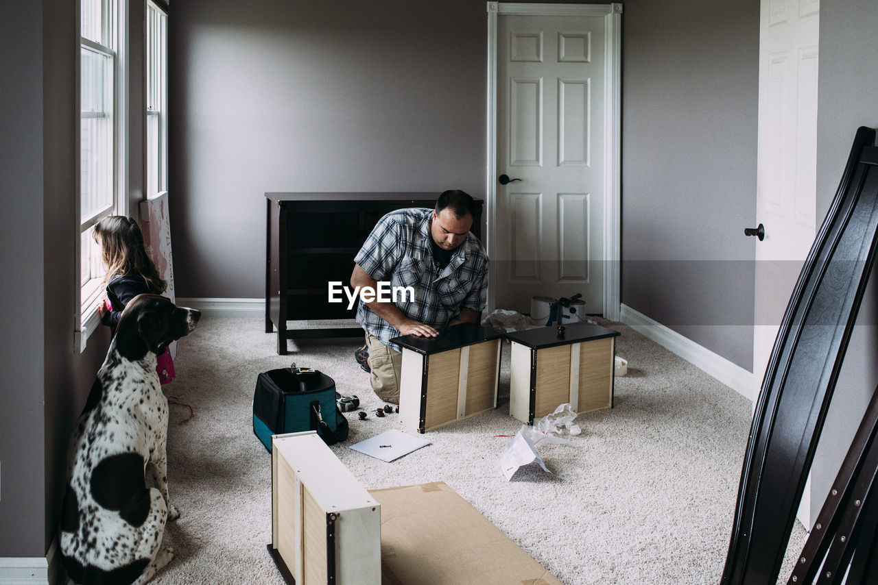 Father repairing drawers while daughter looking through window at home