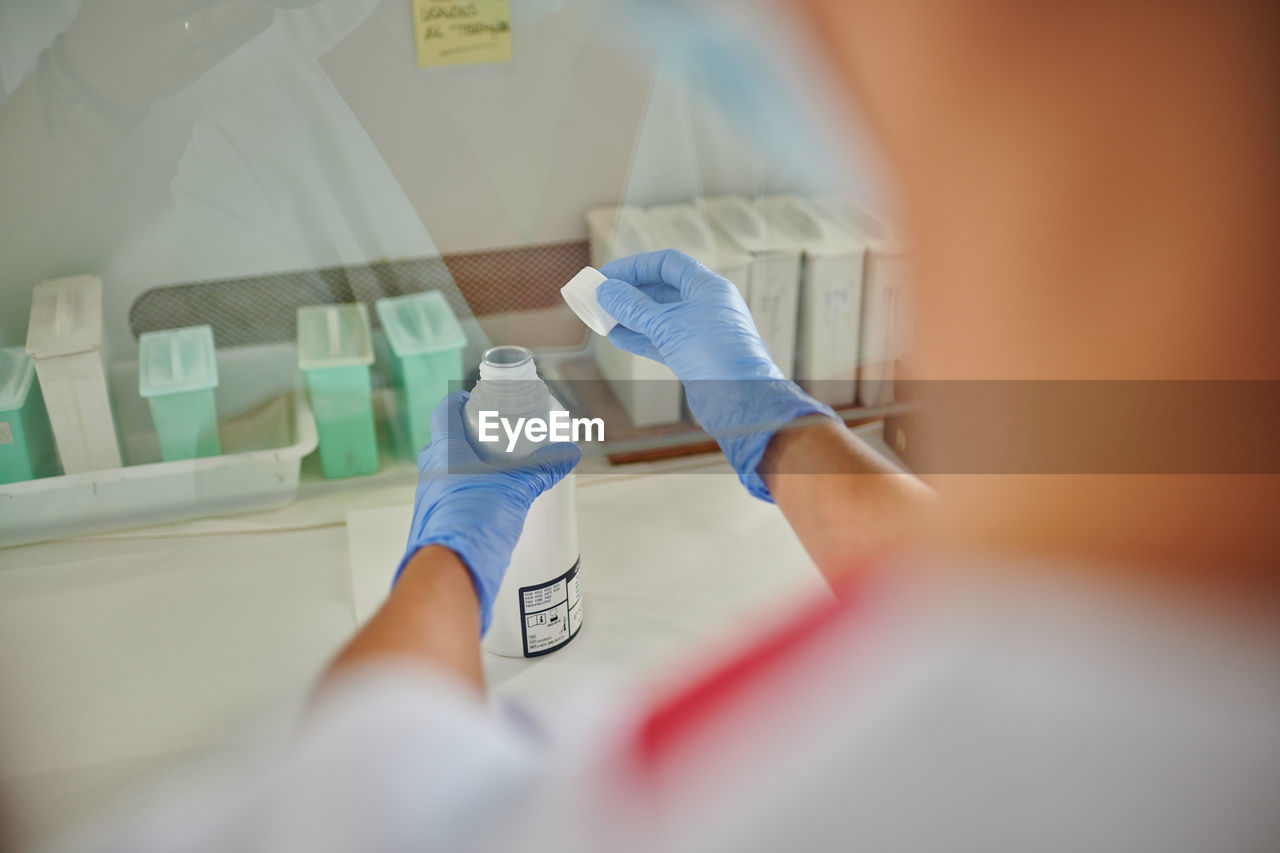 From above back view of crop unrecognizable medical specialist with plastic bottle of liquid near containers in lab