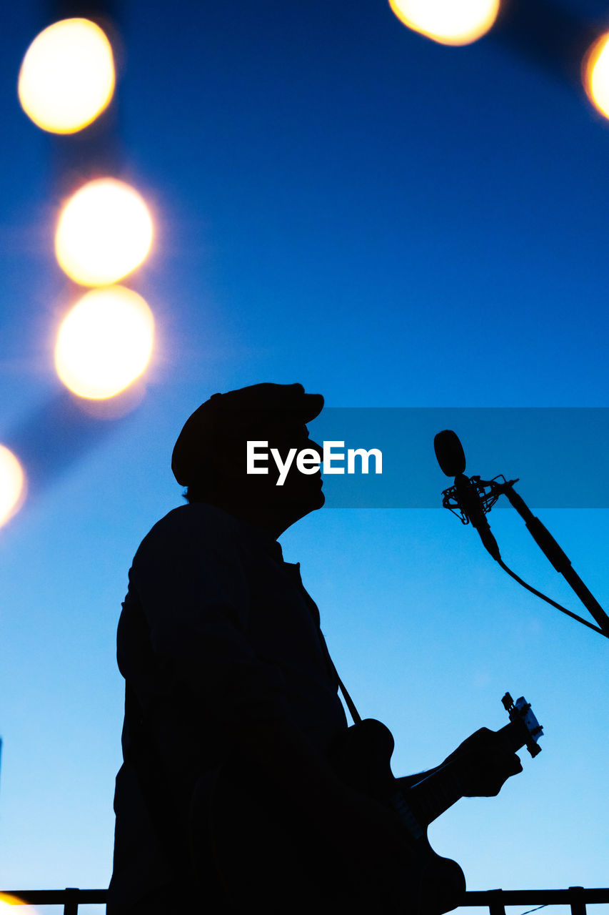 LOW ANGLE VIEW OF SILHOUETTE MAN AGAINST ILLUMINATED BLUE SKY