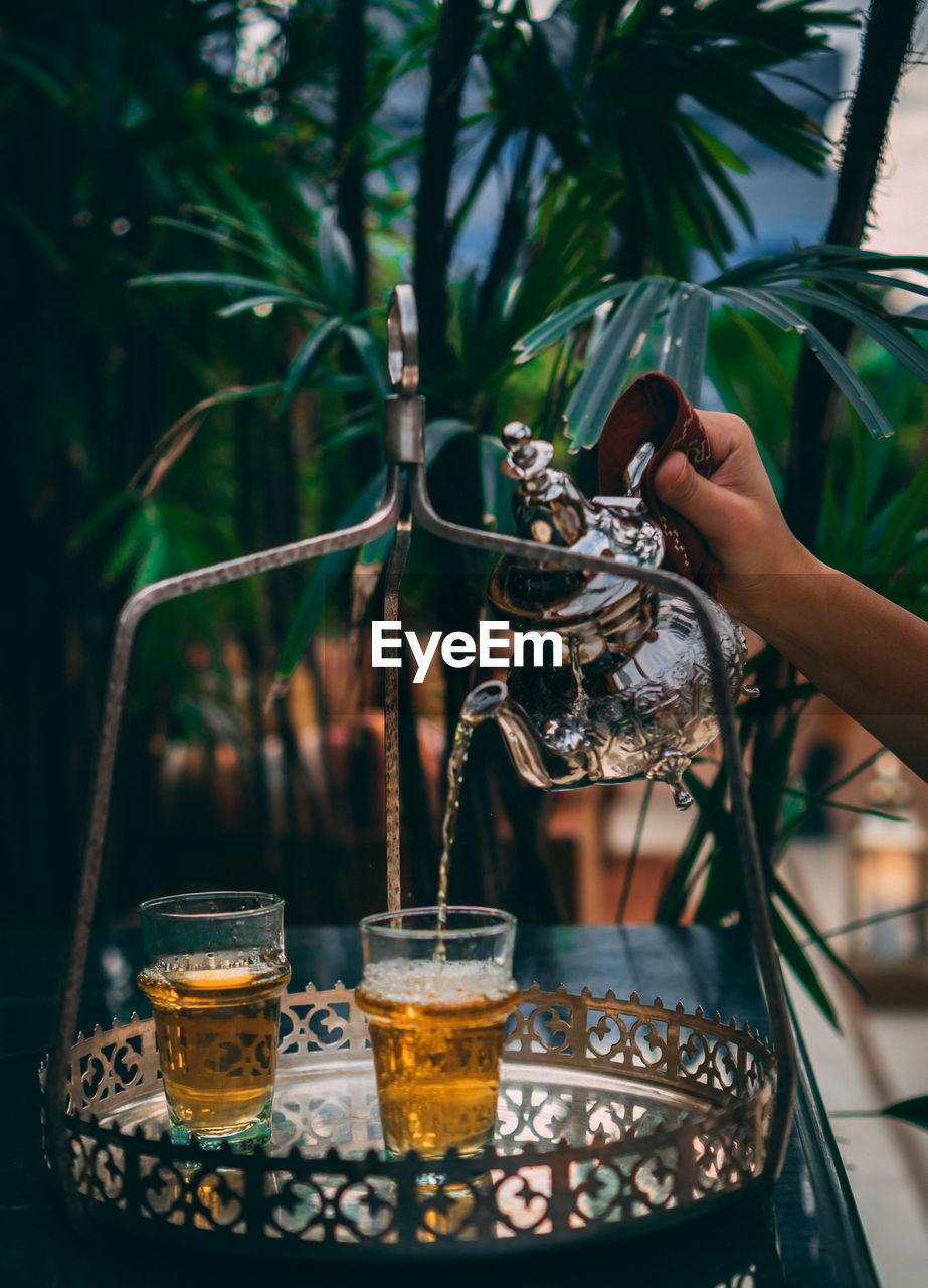 Cropped hand of person pouring drinks in glass outdoors