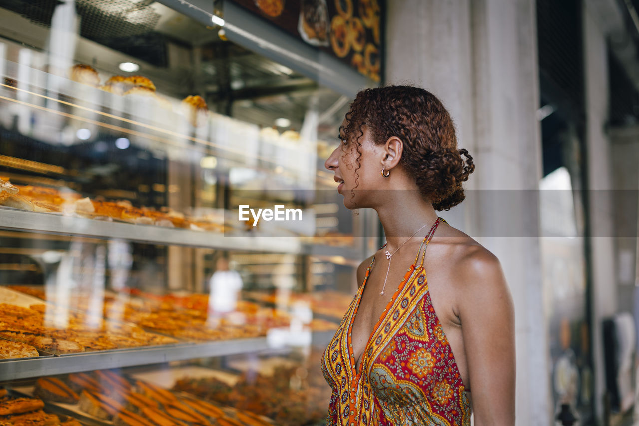 Young woman looking through delicatessen store window