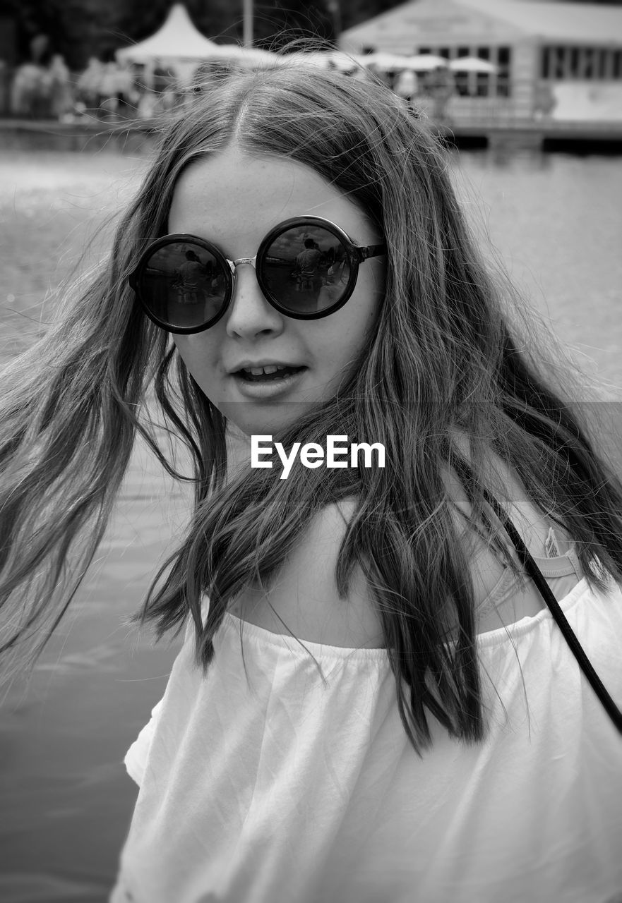 Close-up portrait of young woman wearing sunglasses against lake