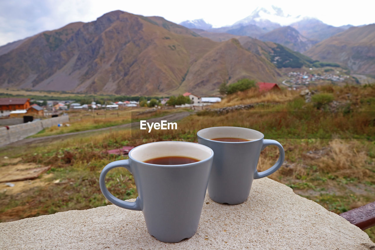 Two cups of on the stone table with blurry countryside view in the backdrop