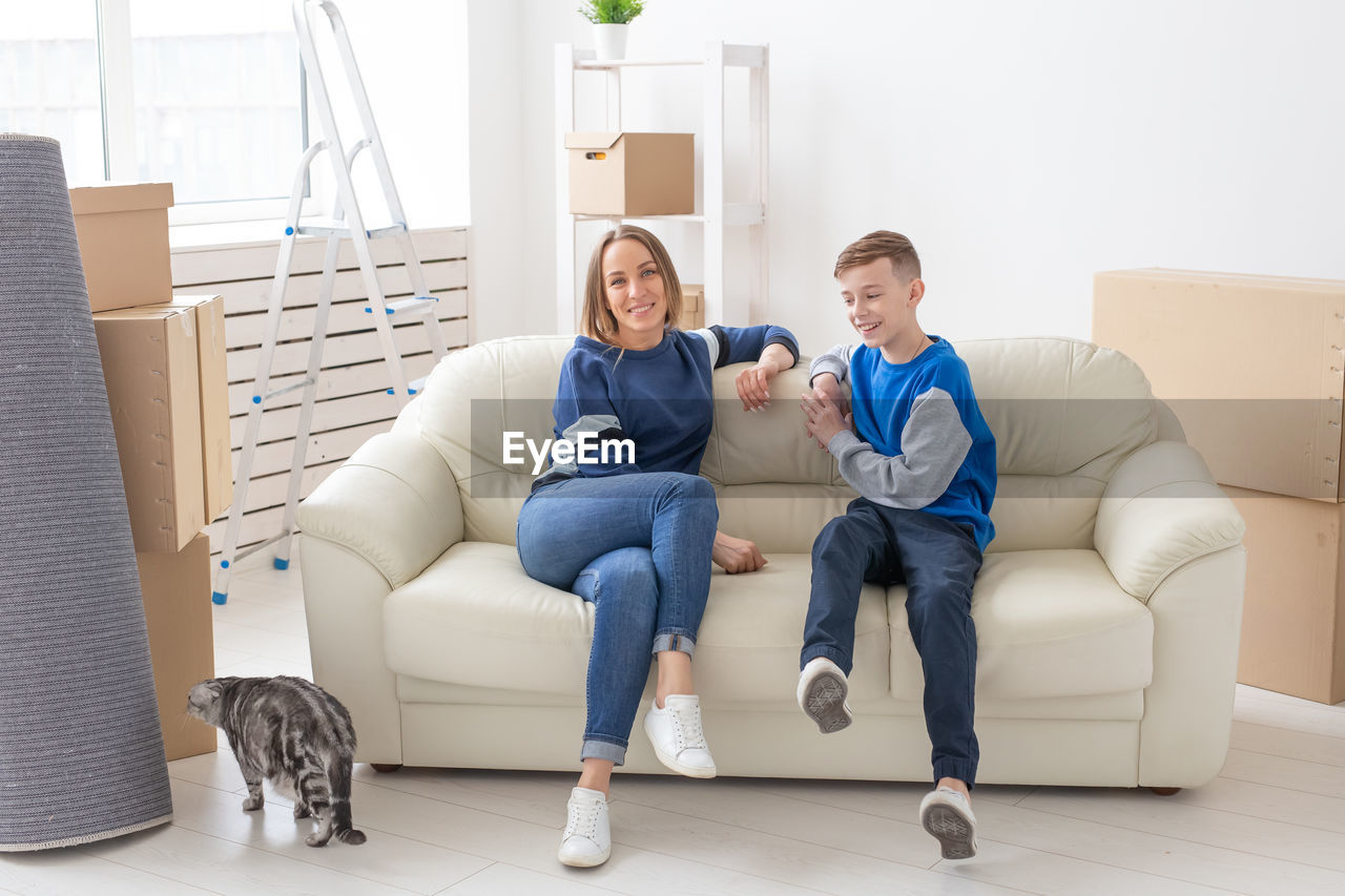 FULL LENGTH OF YOUNG MAN SITTING ON SOFA AT HOME