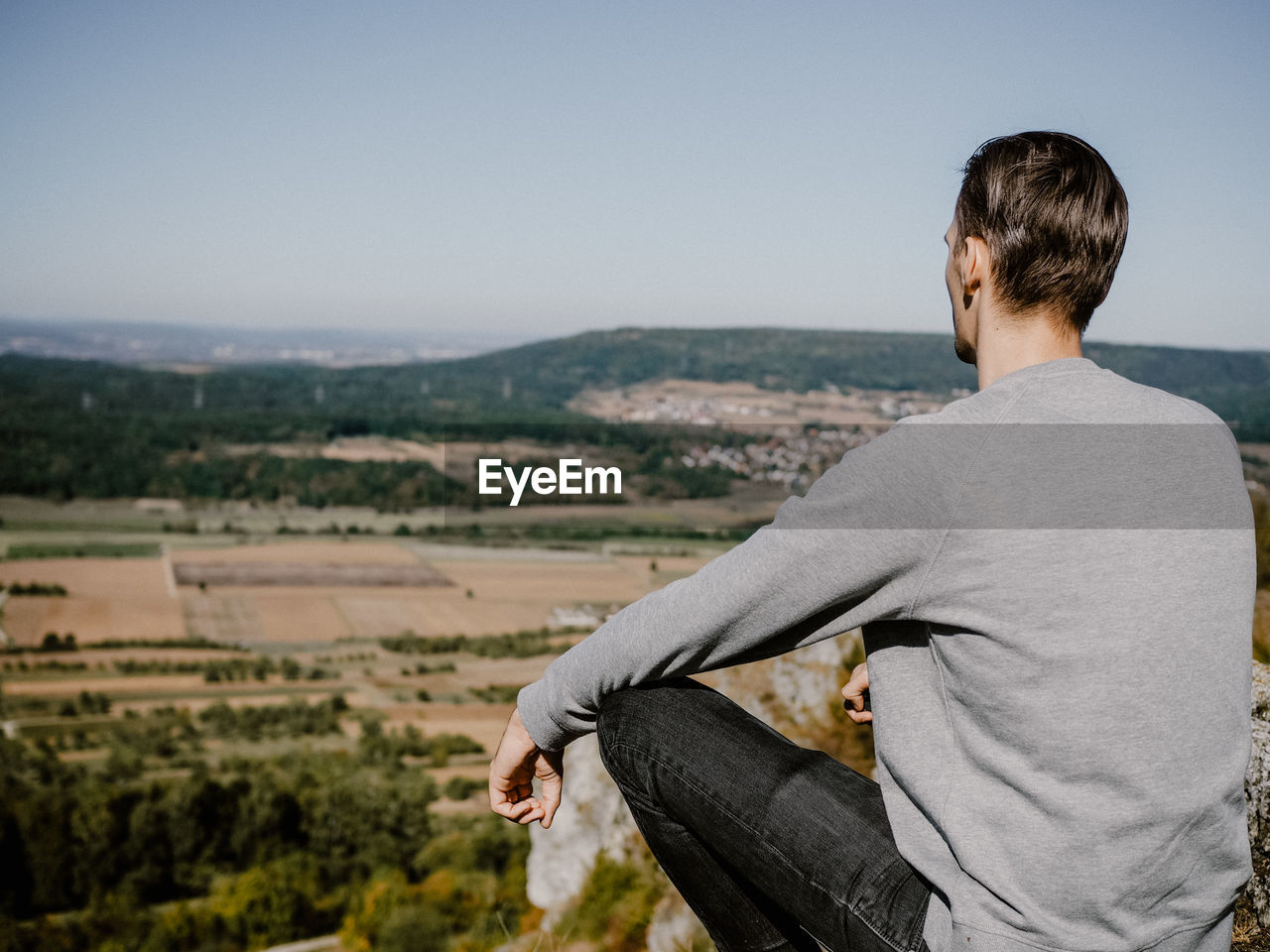 Rear view of man sitting on cliff against sky