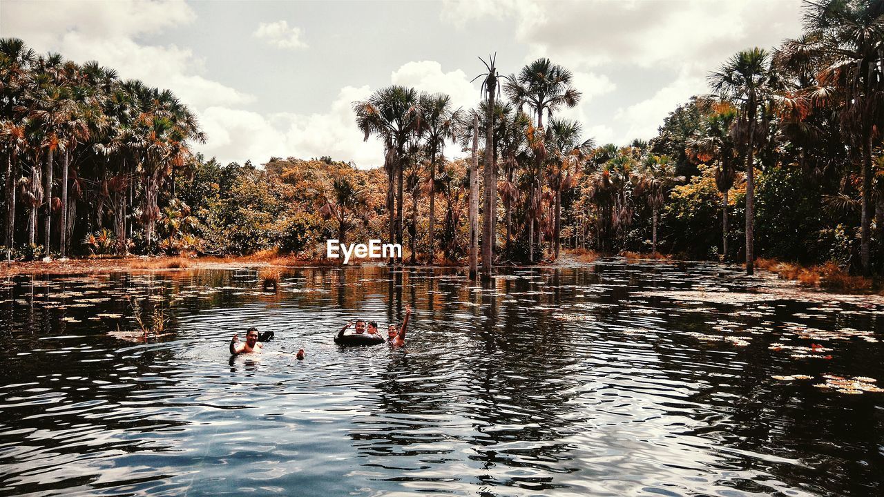 People enjoying in lake by trees