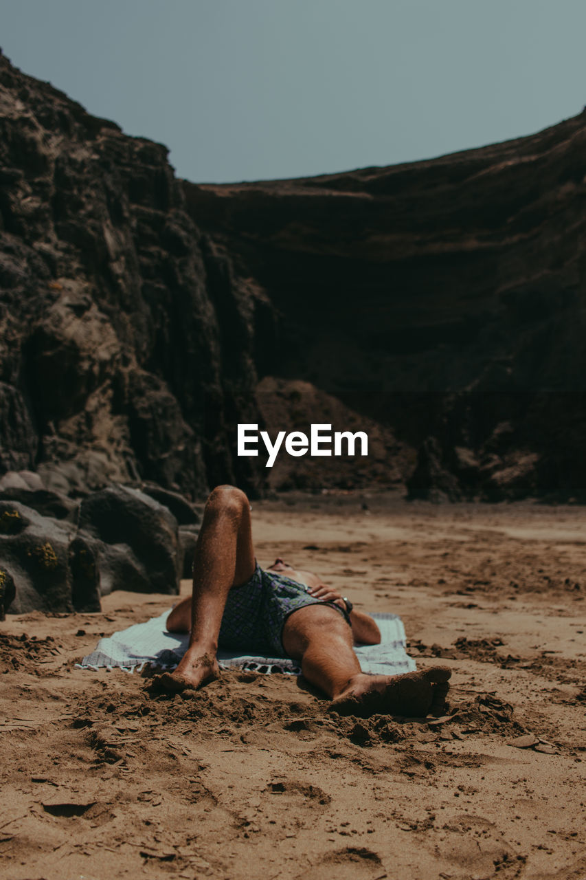 Man lying on sand at beach against rock formations