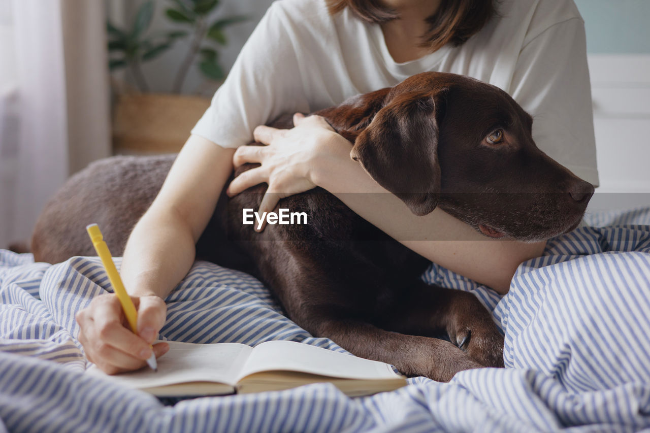 midsection of woman with dog lying on bed at home