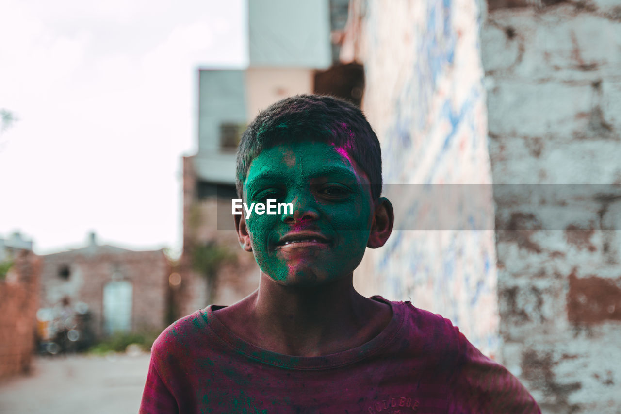 Portrait of smiling boy with green powder paint on face in town during holi