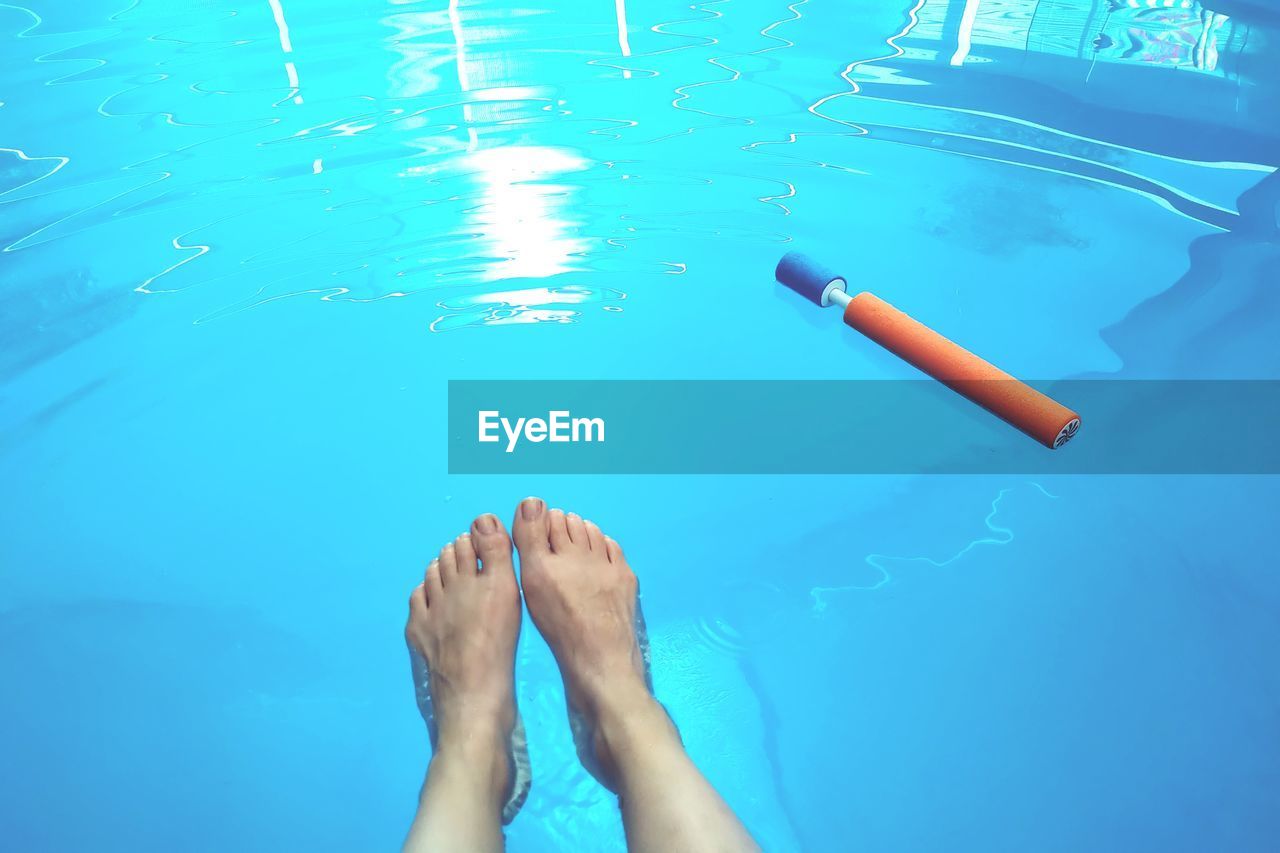 LOW SECTION OF WOMAN LEGS SWIMMING IN POOL