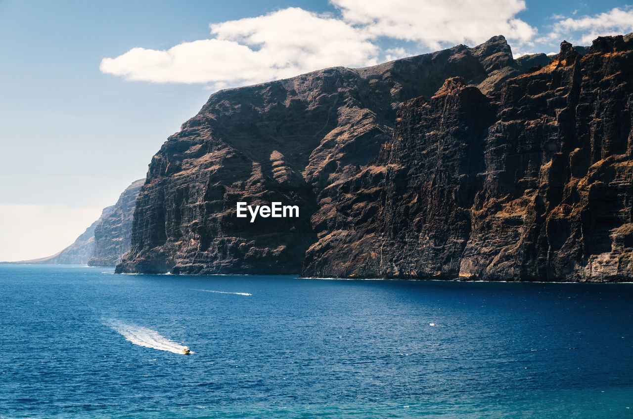 Scenic view of sea by mountain against sky