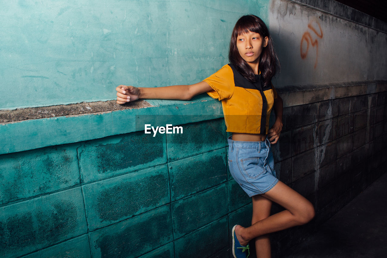 Full length of young woman standing against wall