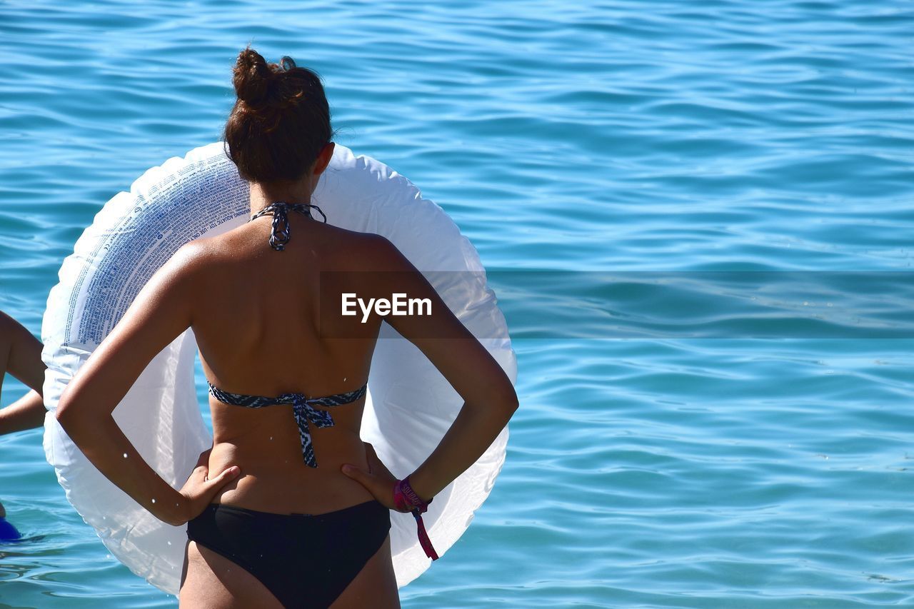 Rear view of shirtless young woman standing in sea