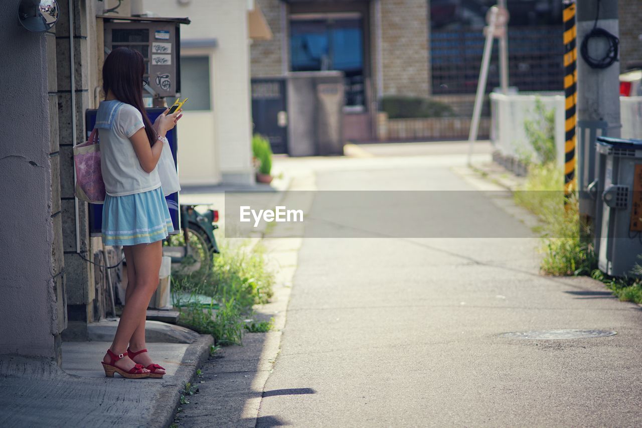 Young woman using phone while standing on footpath