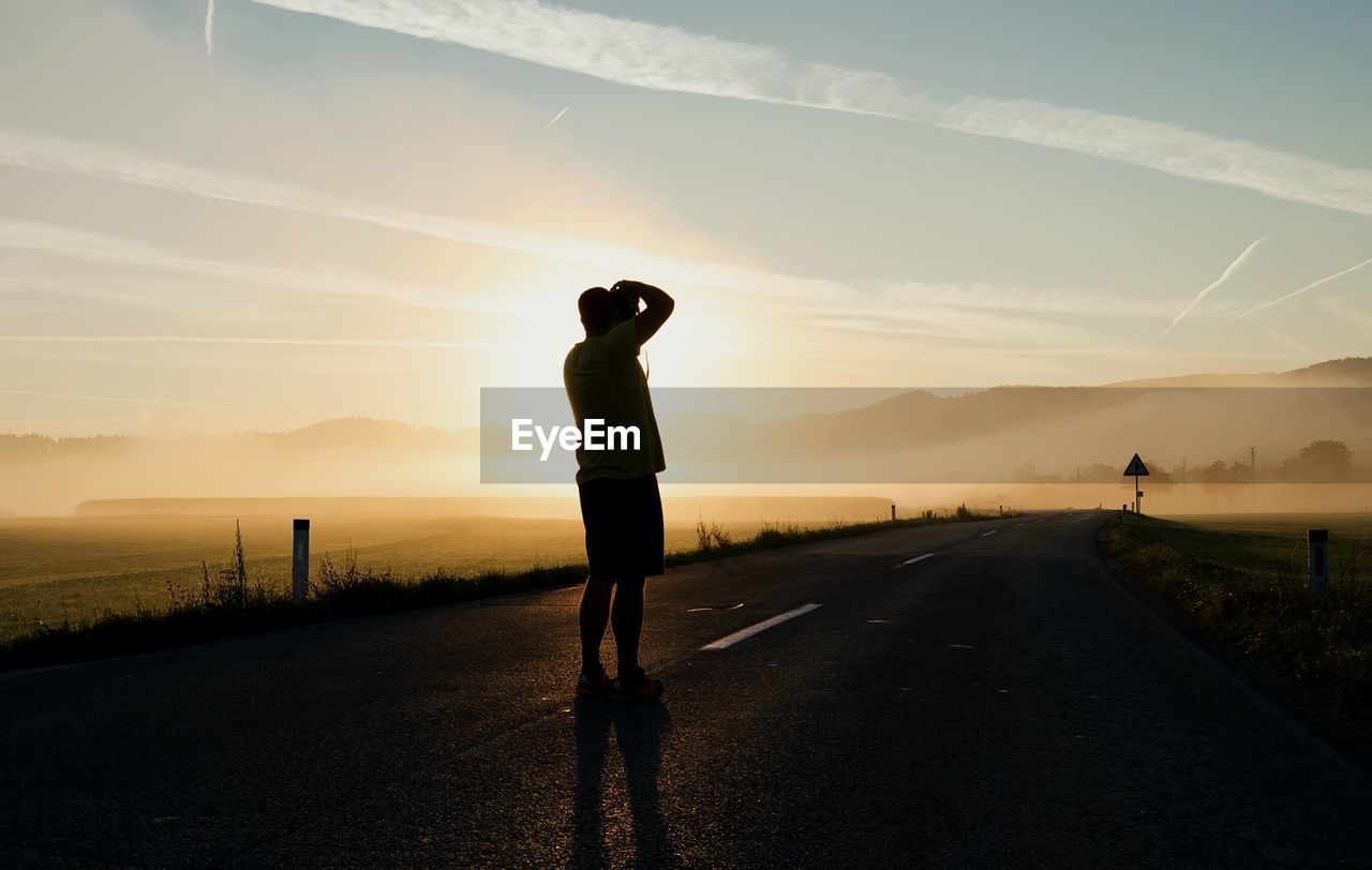 Rear view of man photographing on road during sunset