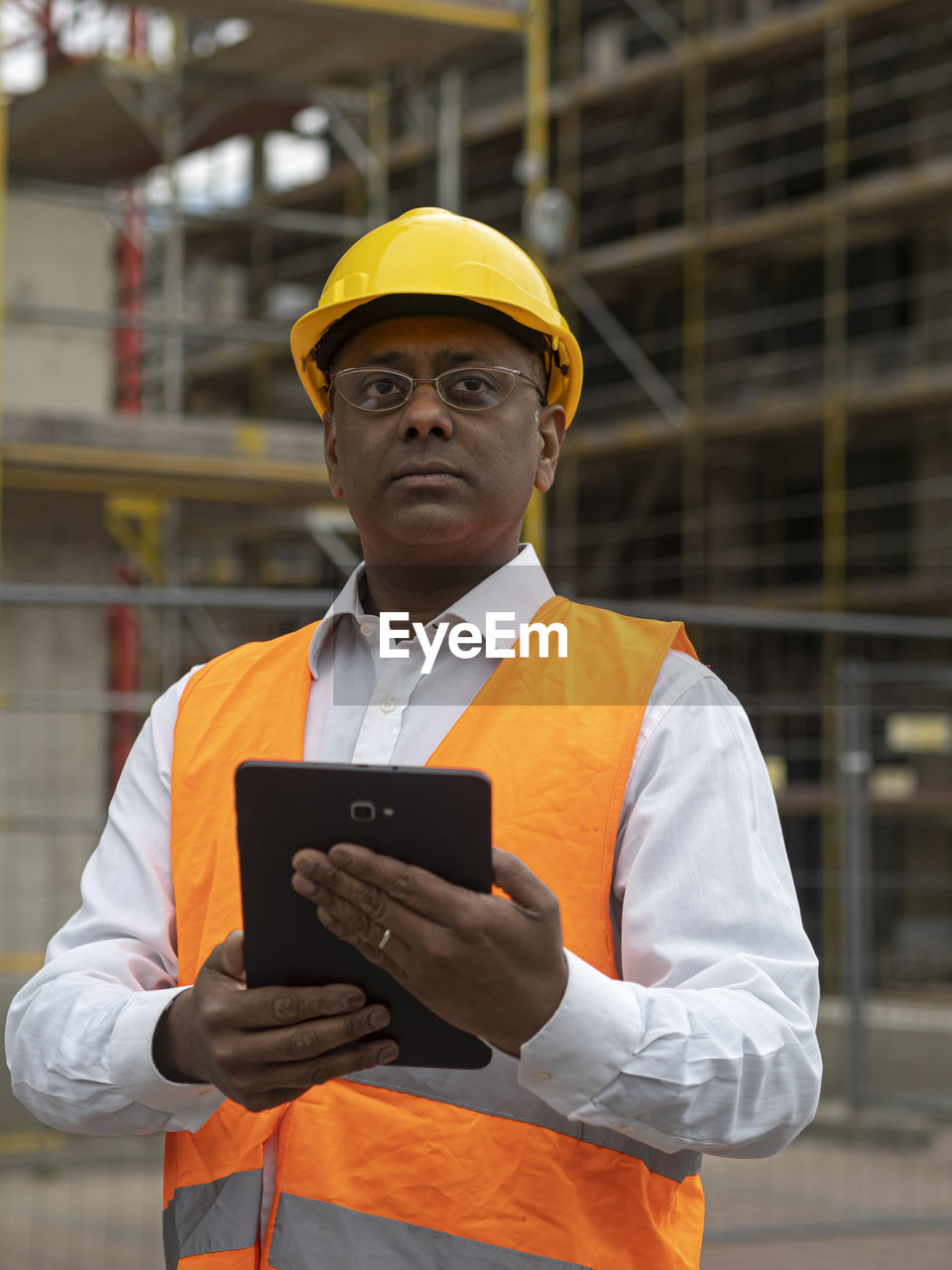 Indian engineer wearing a safety helmet checking documents on a tablet computer on construction site