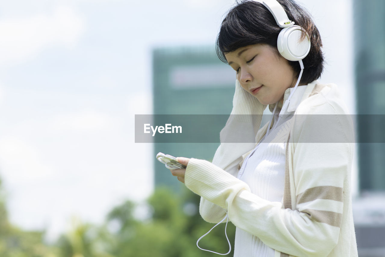 Smiling woman with mobile phone wearing headphones outdoors