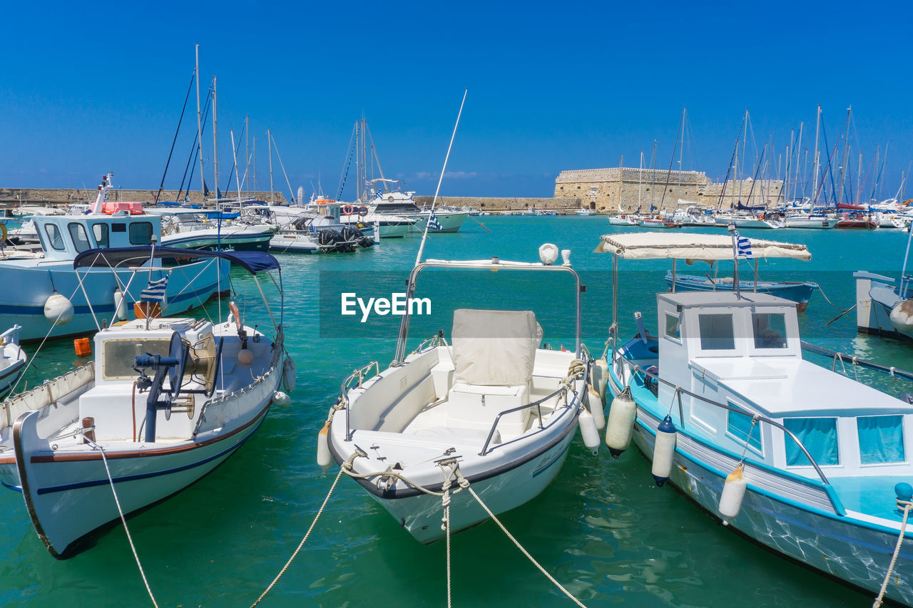 Boats moored in sea against clear blue sky