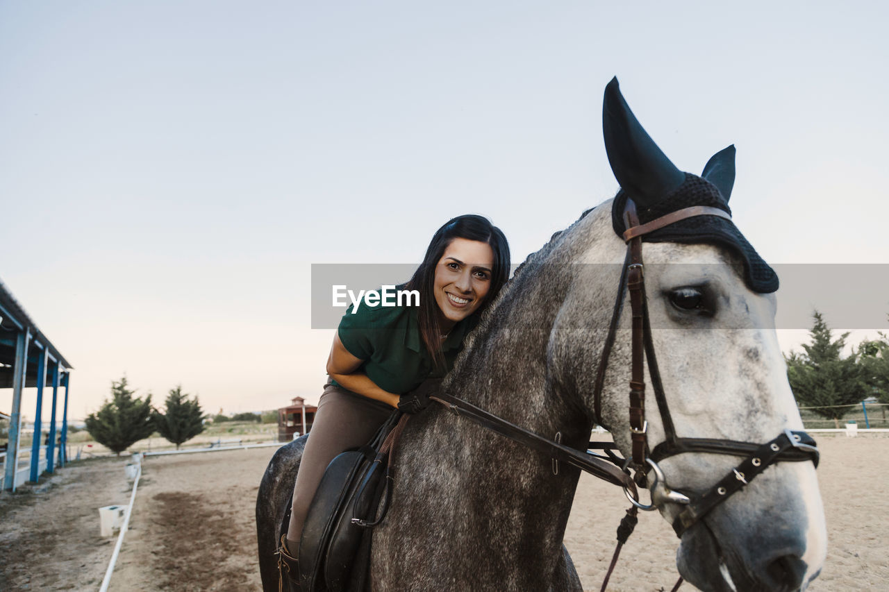 Smiling woman sitting on horse against clear sky at farm