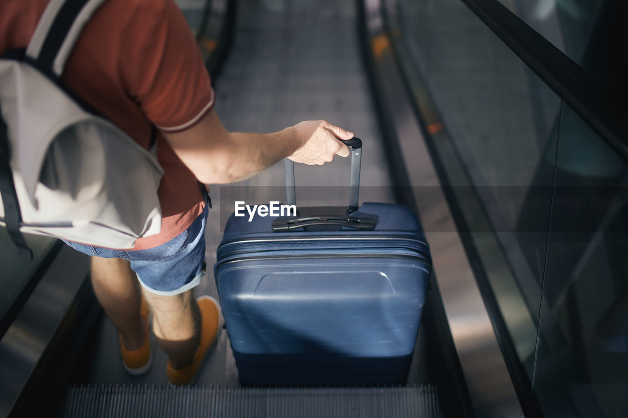 Traveler at airport terminal. rear view of man with suitcase and backpack standing on ecalator. 