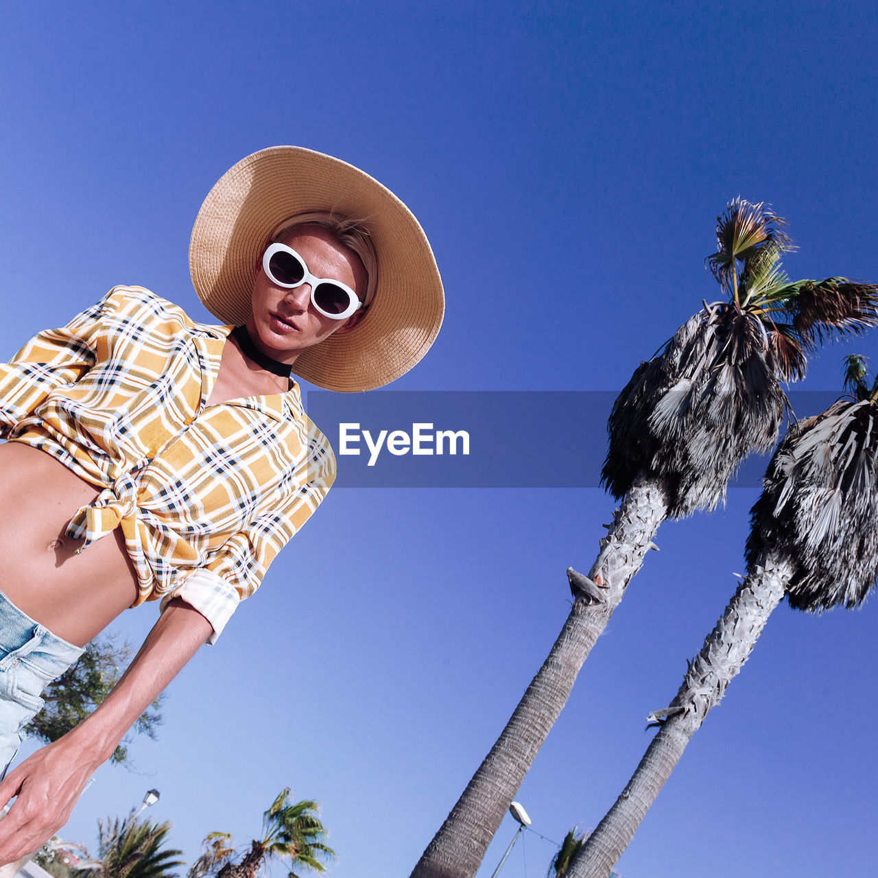 Low angle view of woman by trees against clear blue sky