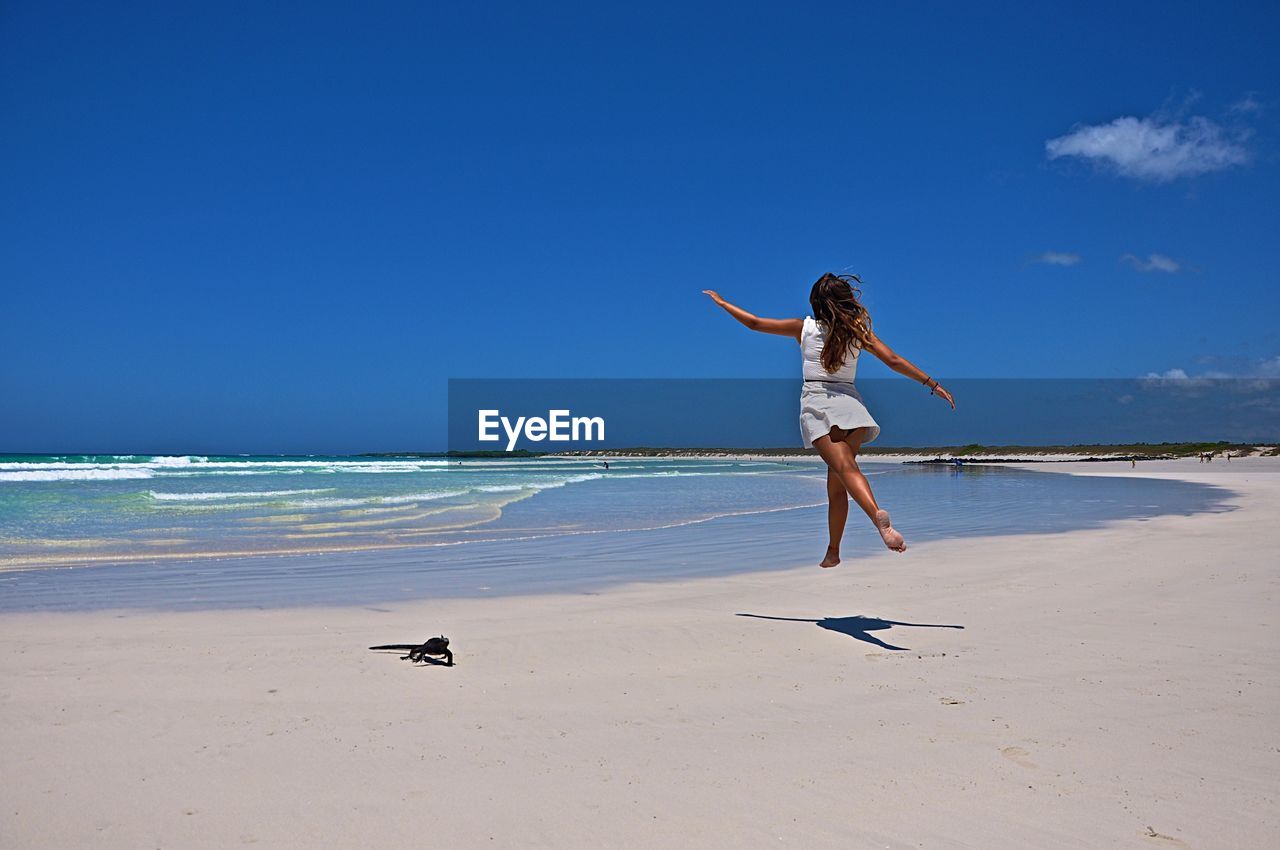 Full length of woman jumping on beach against blue sky