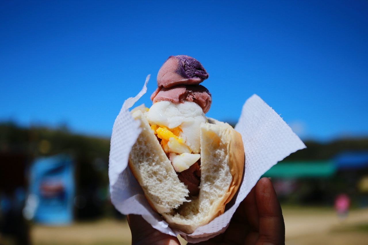 Cropped image of hand holding ice cream sandwich against blue sky