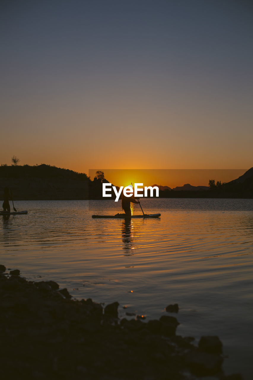 SILHOUETTE PEOPLE ON LAKE AGAINST ORANGE SKY