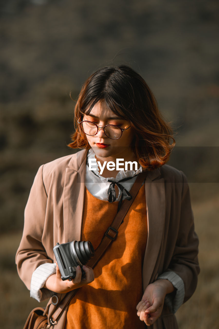 Young woman holding camera while standing outdoors